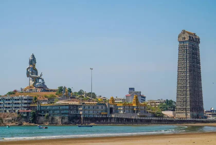 Seaside temple complex with a tall stone tower and Shiva statue